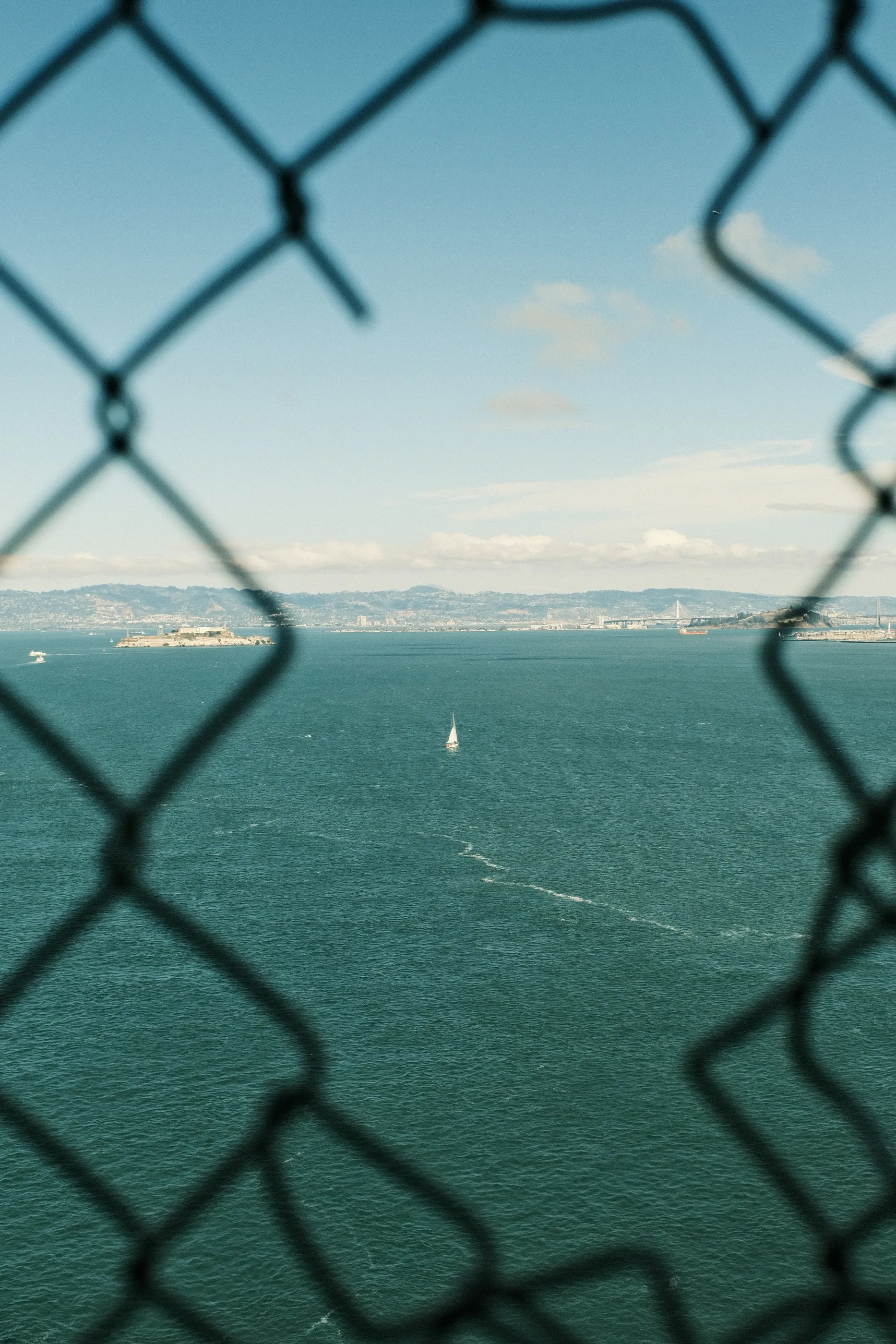 Blue water and distant hills framed by a chain-link fence