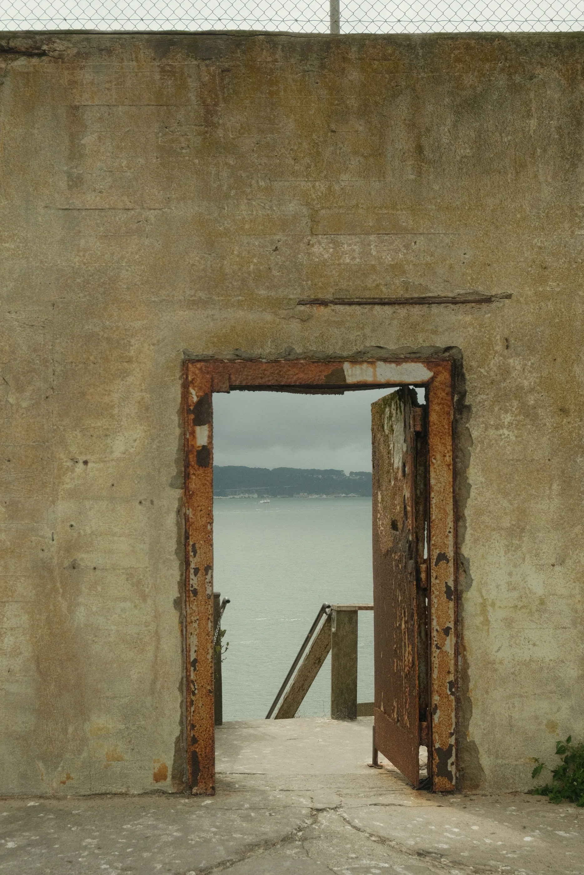 Blue water glimpsed through a rusted doorway in a concrete wall