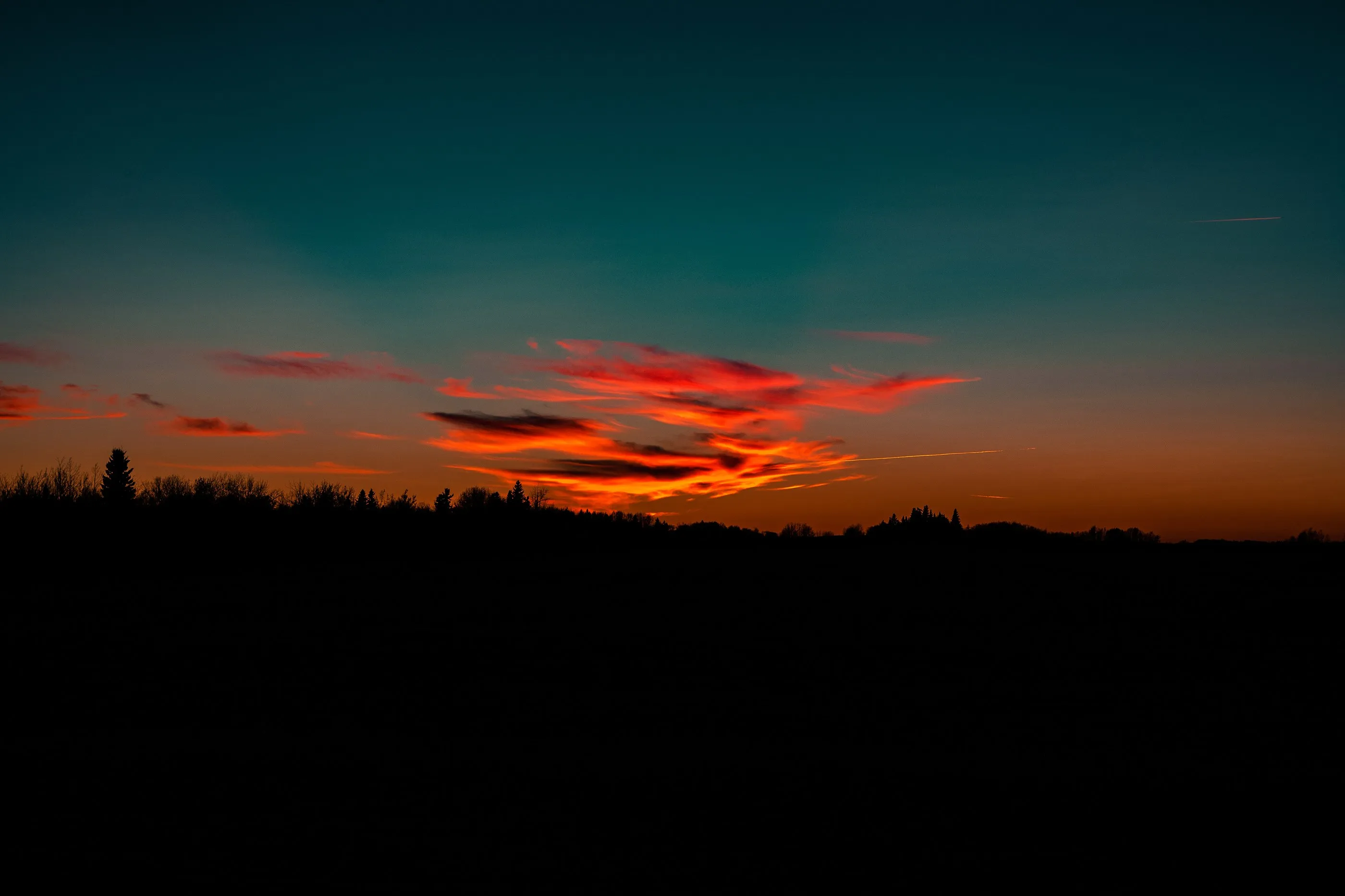 Red streaks of sunset clouds above a dark rural horizon