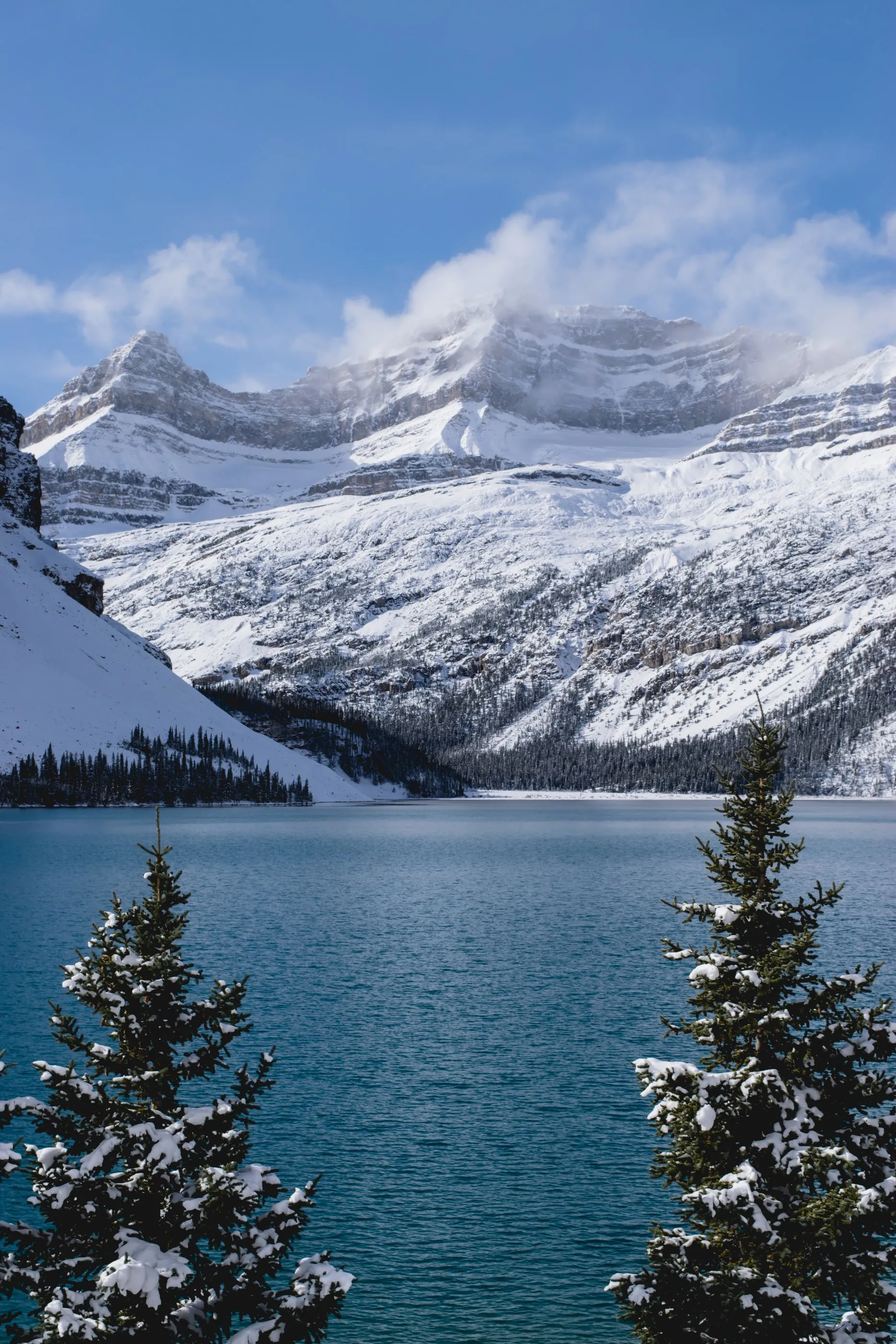 Turquoise mountain water beneath snowy peaks and drifting clouds