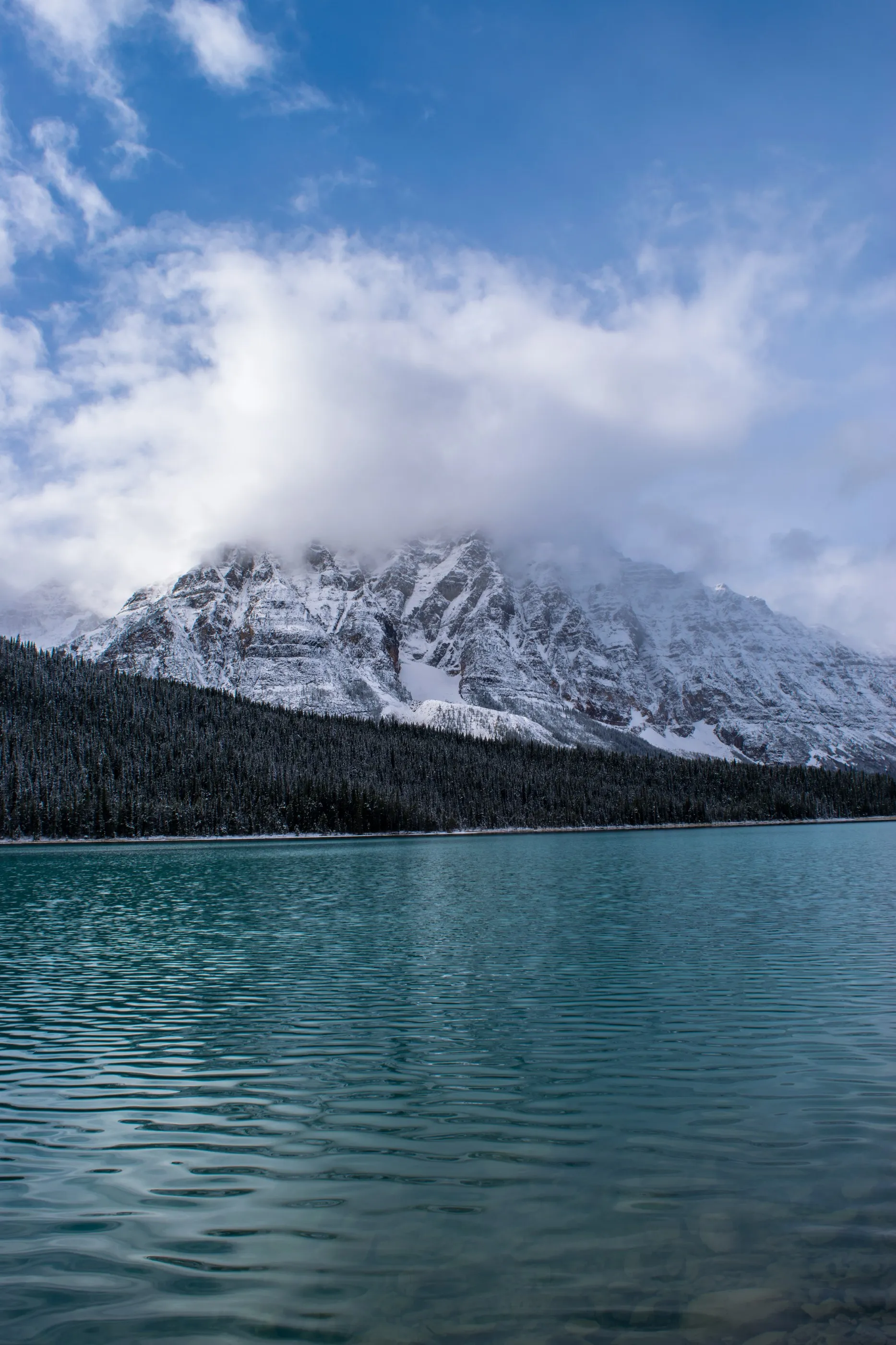 A low cloud obscuring a snow-covered mountain above turquoise water