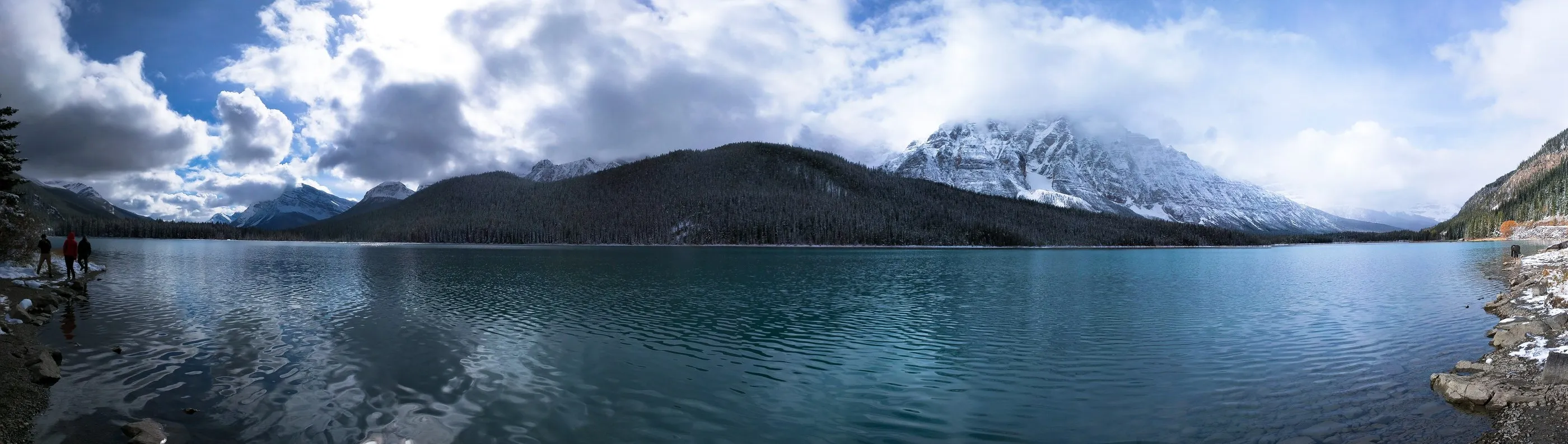 A panoramic mountain lake reflecting dark ridges and clouds