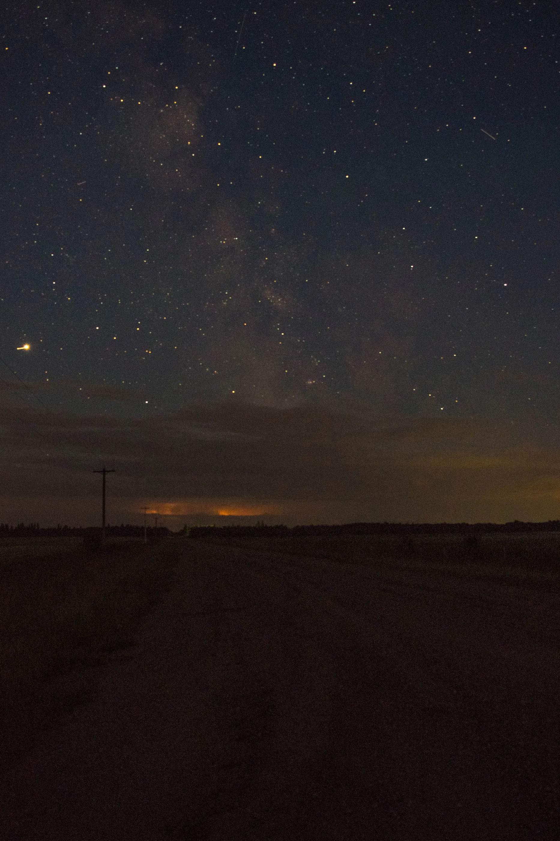 The Milky Way and stars above a dark prairie road and utility poles
